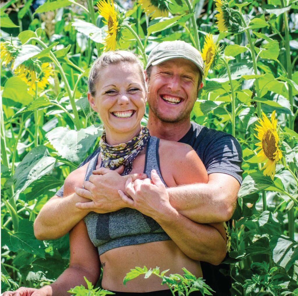 Joy Miller and Rufus Haucke of Driftless Curiosity stand in a field of sunflowers 