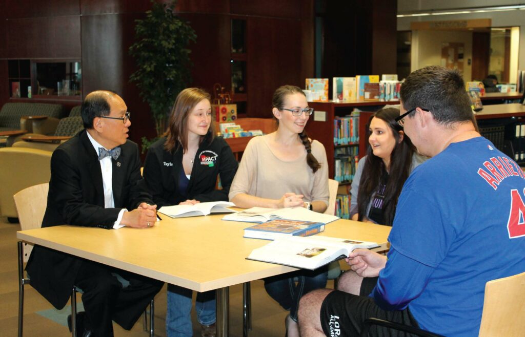 Liang Chee Wee sits at a table talking with several students at NICC